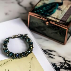 A close-up of a stylish gemstone bracelet resting on a marble surface beside a decorative box.